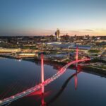 Wide-angle view of the Bob Kerrey Pedestrian Bridge connecting Omaha, Nebraska, and Council Bluffs, Iowa, over the Missouri River under a clear sky.